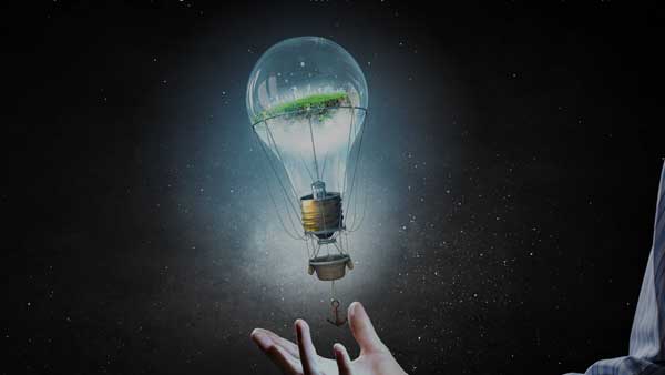 Eine Hand, die eine Glühbirne hält, in dieser befinden sich Symbole von Alternativenergie